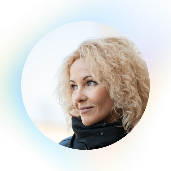 A woman with curly blonde hair and blue eyes looks to the side, wearing a black scarf. The background is softly blurred with a light, pastel color gradient.